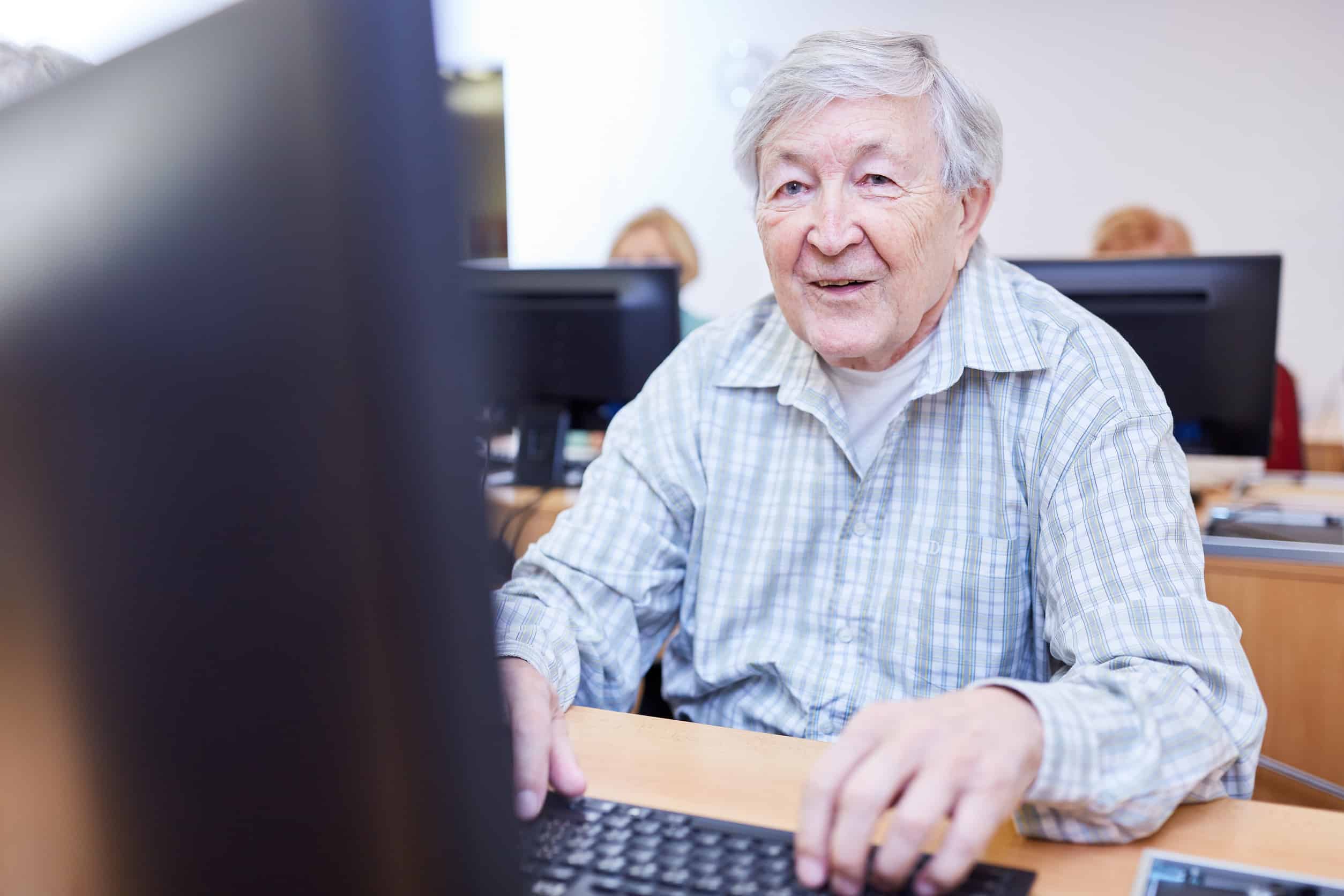 Older adults in a retirement home sit on a PC in a computer course